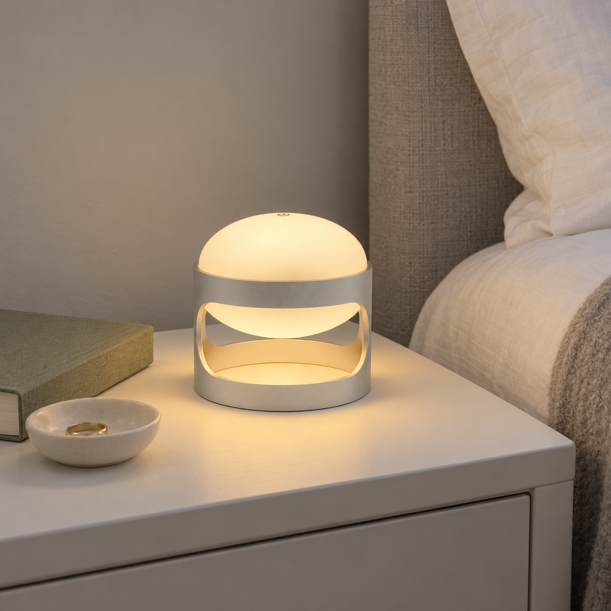 Lotus Mini cordless lamp in Matte Silver, lit on a white bedside table