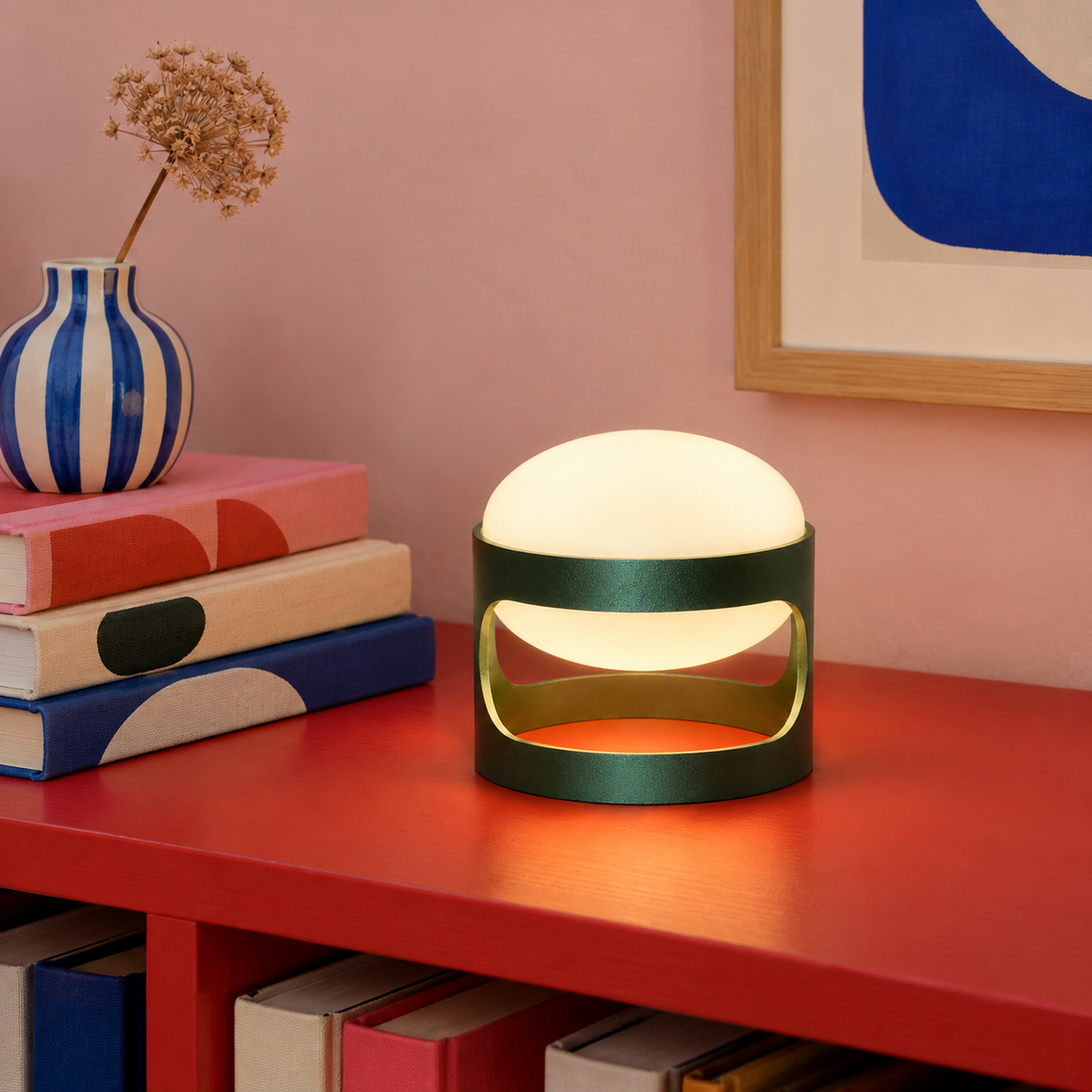 Lotus Mini cordless lamp in Deep Forest Green, lit on a red bookshelf