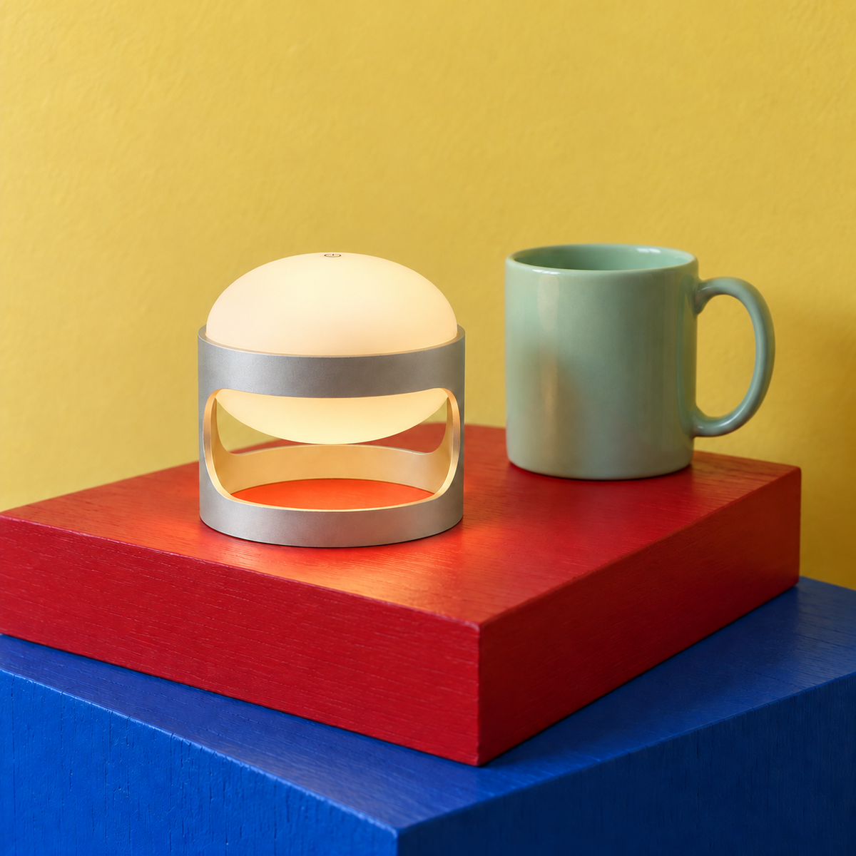 Lotus Mini cordless lamp in Matte Silver on red and blue blocks beside a mint mug for scale