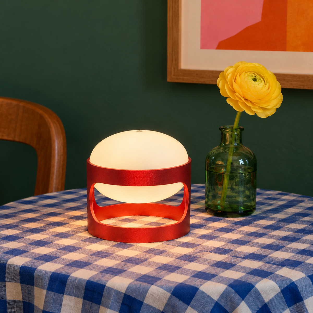 Lotus Mini cordless lamp in Deep Red on a blue gingham table with a yellow flower