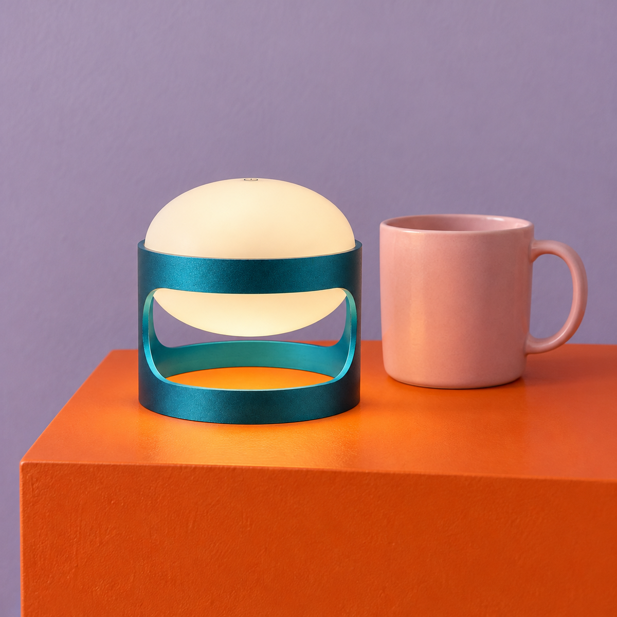 Lotus Mini cordless lamp in Deep Teal Blue on an orange block beside a pink mug for scale